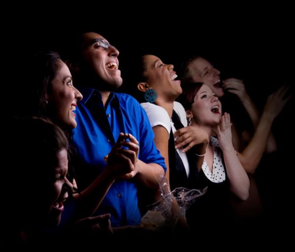 Photo of a row of adults laughing at something out of our view. The background is darkened, like they're in a theatre watching a performance