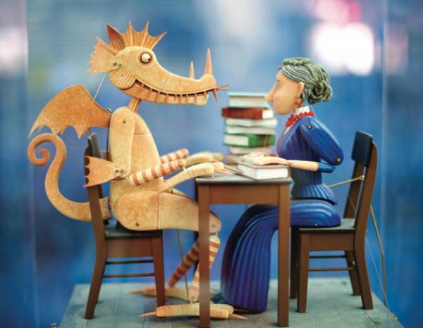 Wooden figurine of a woman sits across a desk from a wooden figurine of a dragon