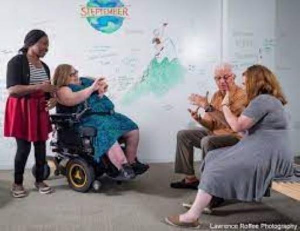 Photo of several people communicating in ASL, including a woman in a powered wheelchair