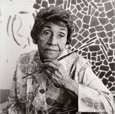 Alma W. Thomas posing with a paintbrush in front of one of her paintings