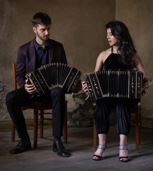 two people seated, both playing the accordion 