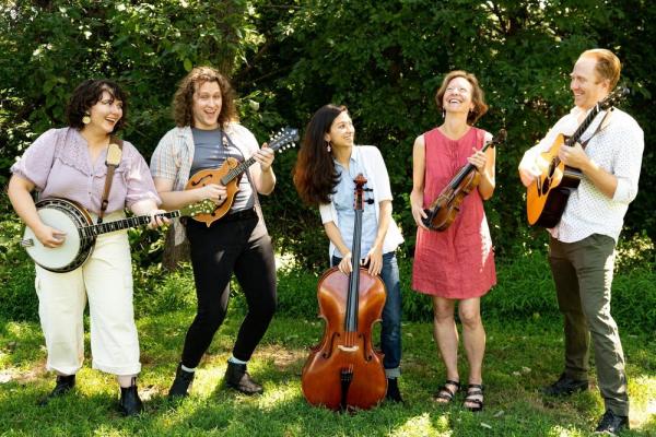 5 musicians stand in the grass with their stringed instruments