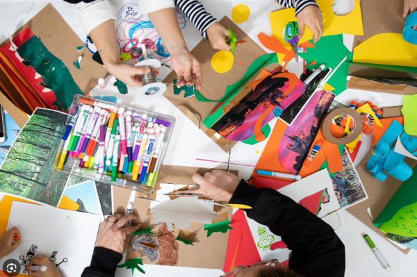 Hands reaching out to do crafts with a variety of art supplies on a table