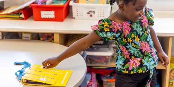 Young girl reaches behind her to touch a yellow book on a table
