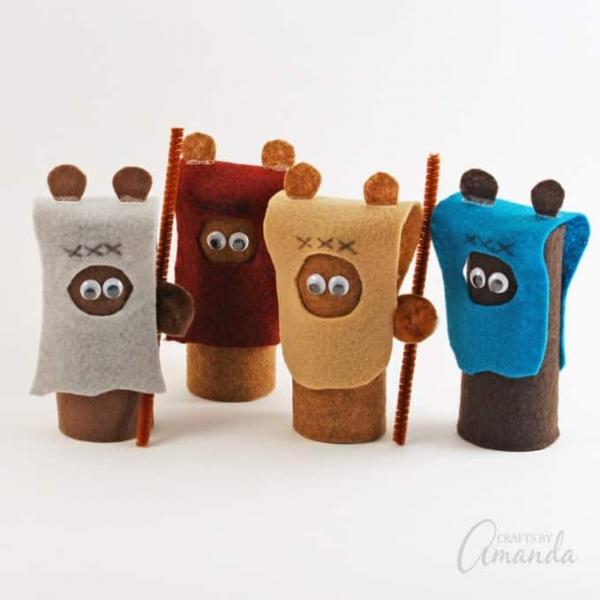 Four Ewoks made from cardboard tubes, each wearing a different colored headwrap. Gray, dark brown, tan, and blue. Two of them are holding pipe cleaner spears.