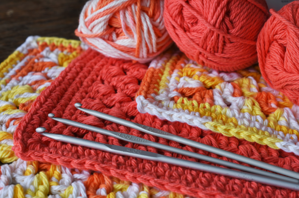 Yarn, crochet needles, and crochet works in coral, yellow, and white colors