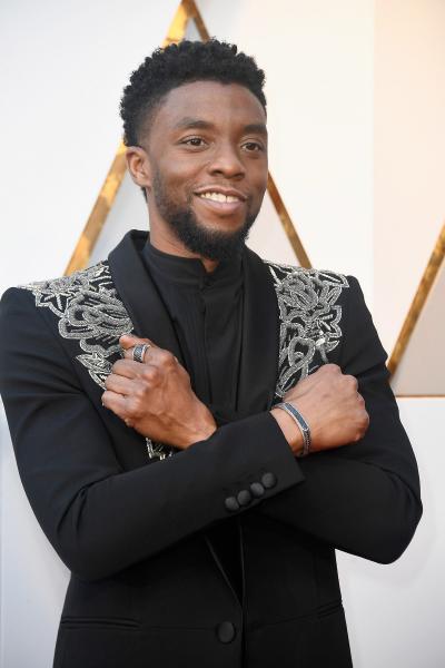 Actor Chadwick Boseman at an award ceremony standing with arms crossed over his chest, the Wakanda Forever symbol.