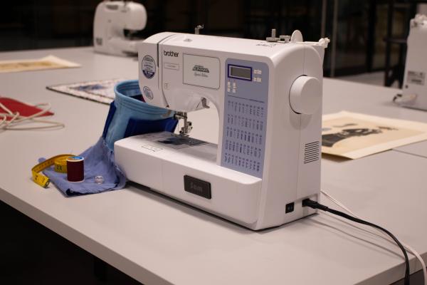 A Brother sewing machine on a white table and a bucket of sewing notions.
