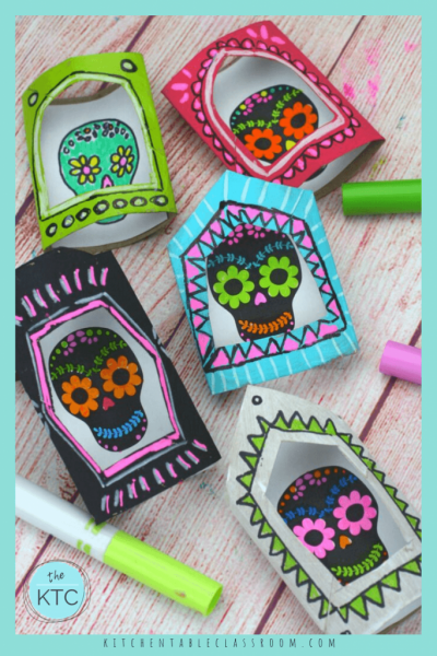 Five brightly colored nicho boxes made from cardboard tubes with sugar skulls inside them.