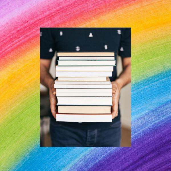 Person holding stack of books in front of a painted rainbow