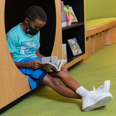 photo of child sitting in a cubby reading a book