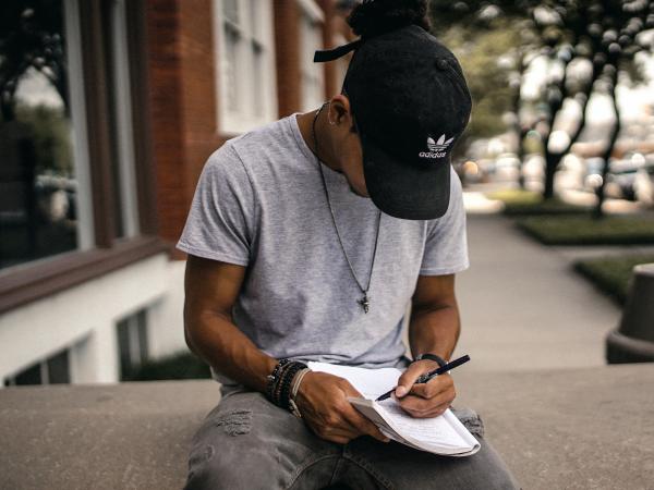 Young person wearing a hat sits with a notebook and pen