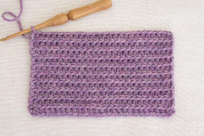 A skein of purple yarn that has been crocheted with a wooden crochet hook.