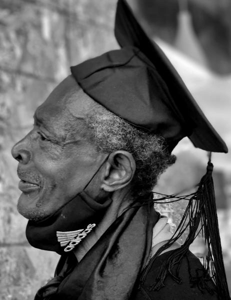black and white image of an older man in a graduation cap and mask pulled down under his chin