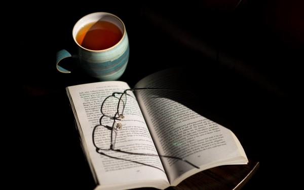 Photograph of cup of tea with open book and glasses resting on the page