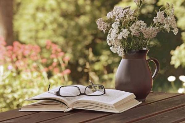 a pair of glasses rests on an open book next to a vase of flowers