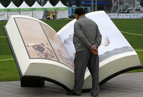 man stands with his hands behind his back looking at a lifesize book