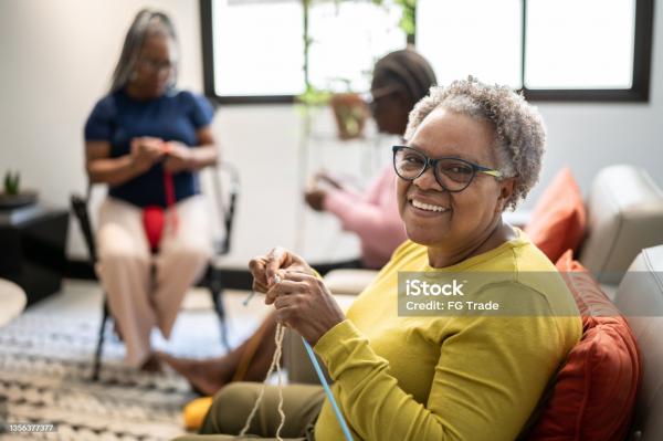 three women sit in a living room knitting 