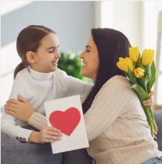child hugs mom with a card and bouquet of yellow tulips