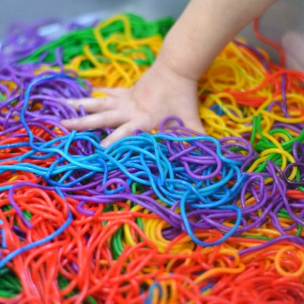 child's hand playing with rainbow spaghetti