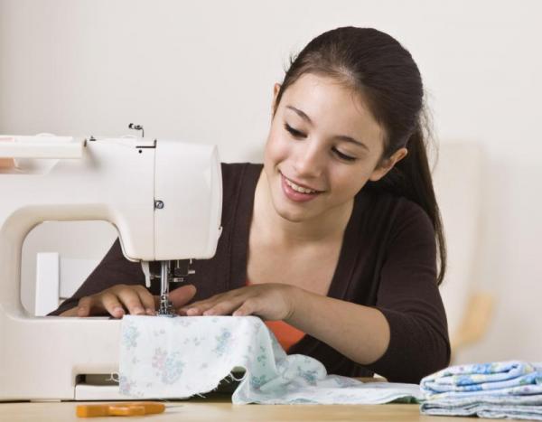 A dark-haired girls sits and uses an electric sewing machine.