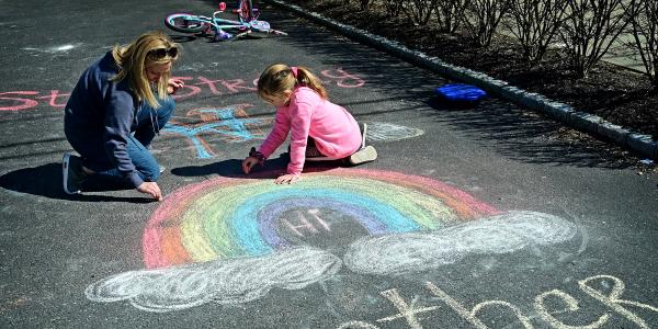 photo of parent and child drawing a rainbow with chalk on the sidewalk