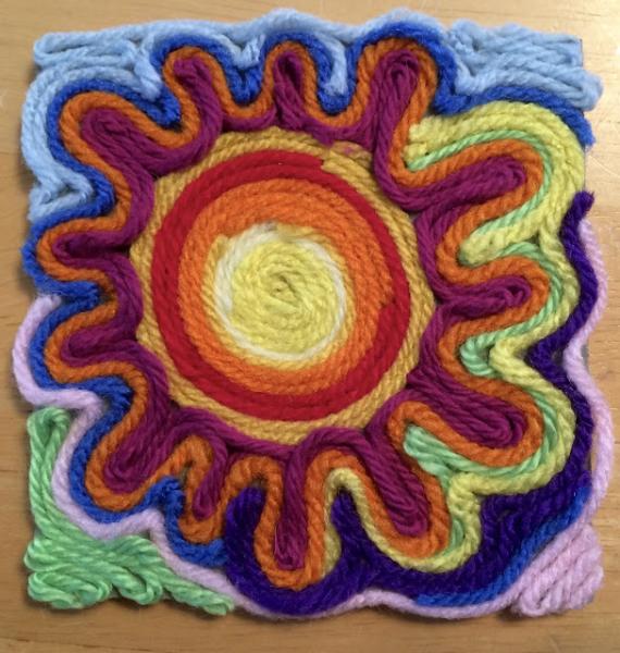 artwork of a sun made out of yarn laid flat on a board